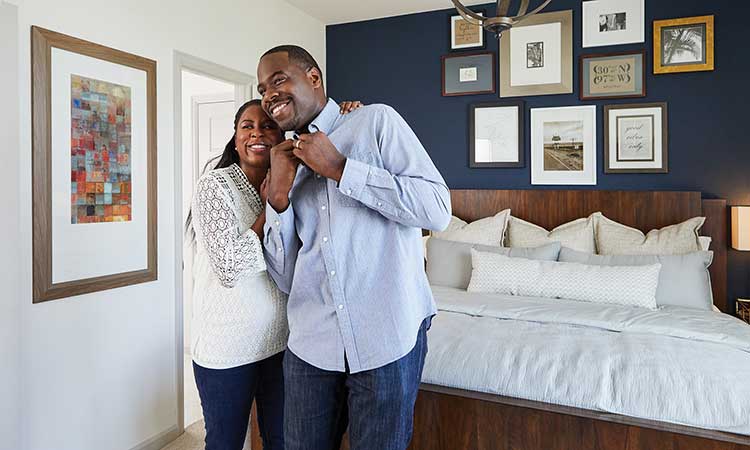 a man and woman stand in a bedroom smiling