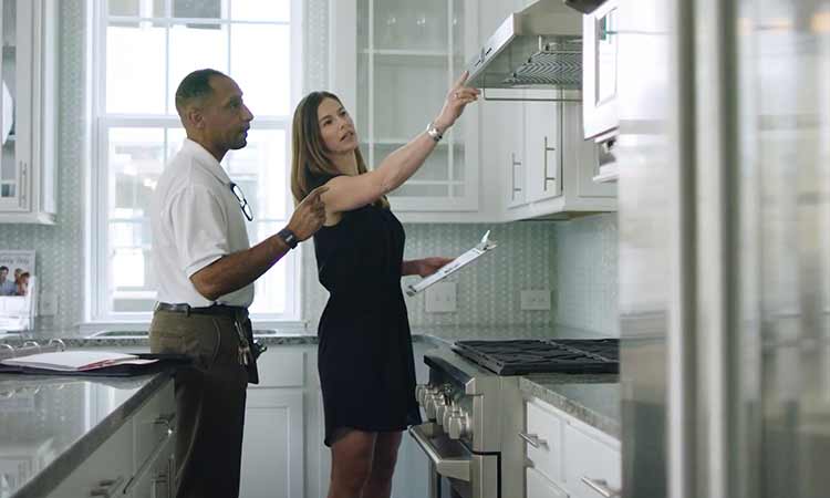 A David Weekley Homes Team Member and a customer look at a kitchen cooktop