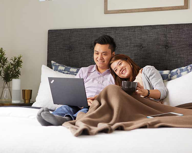 man and woman sitting in bed looking at a laptop