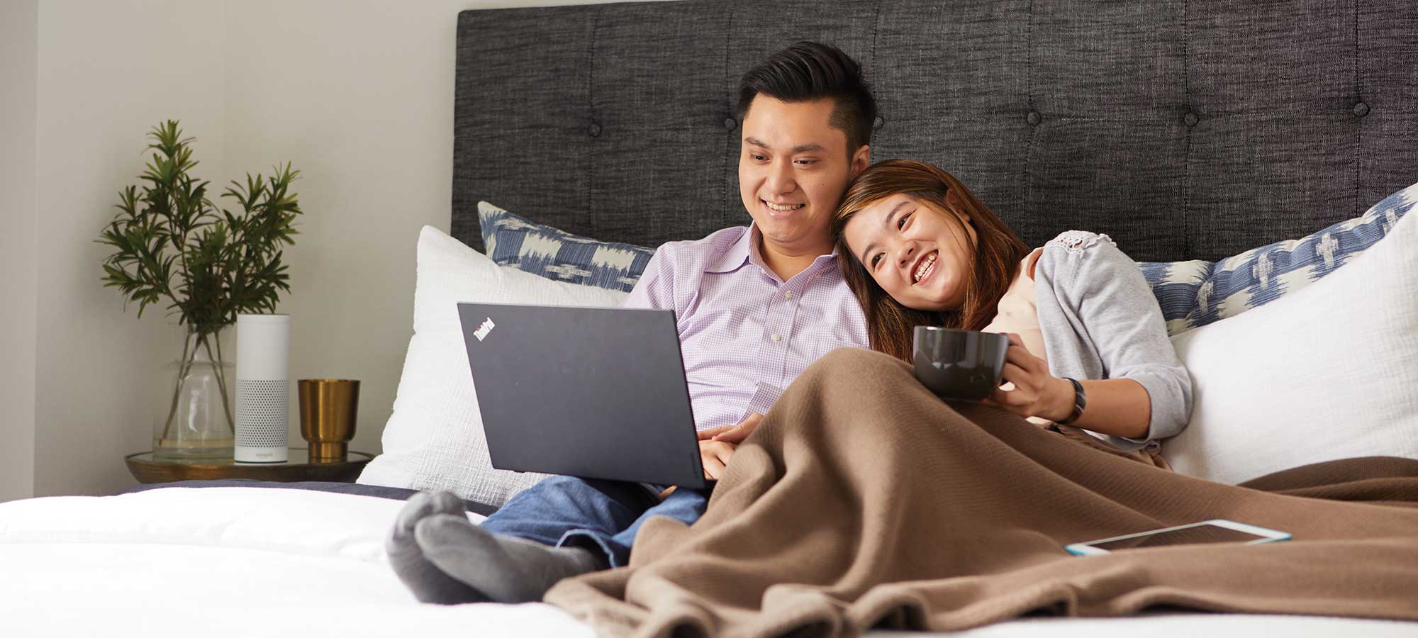a man and woman sitting in bed looking at a laptop