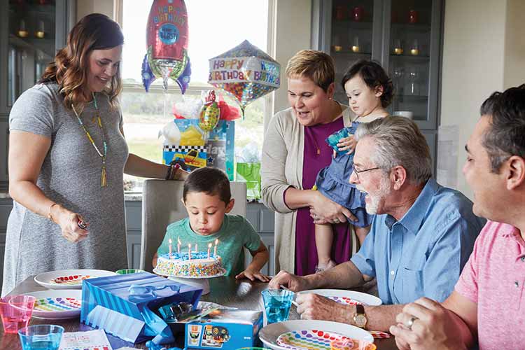 a family gathers around a table while a young boy blows out candles on a birthday cake